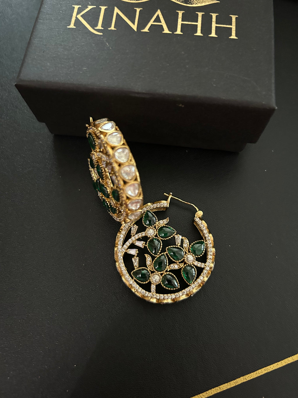 Chaand circular brass hoop earrings with green teardrop stones and moissanite polki, photographed beside a KINAHH box.