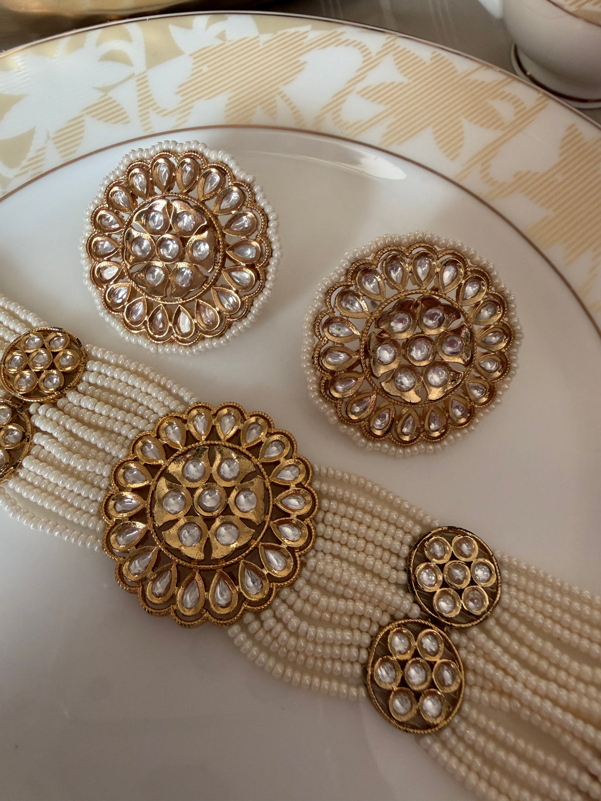Close detail of Renuka gold-tone floral motifs, ivory pearl strands and matching stud earrings