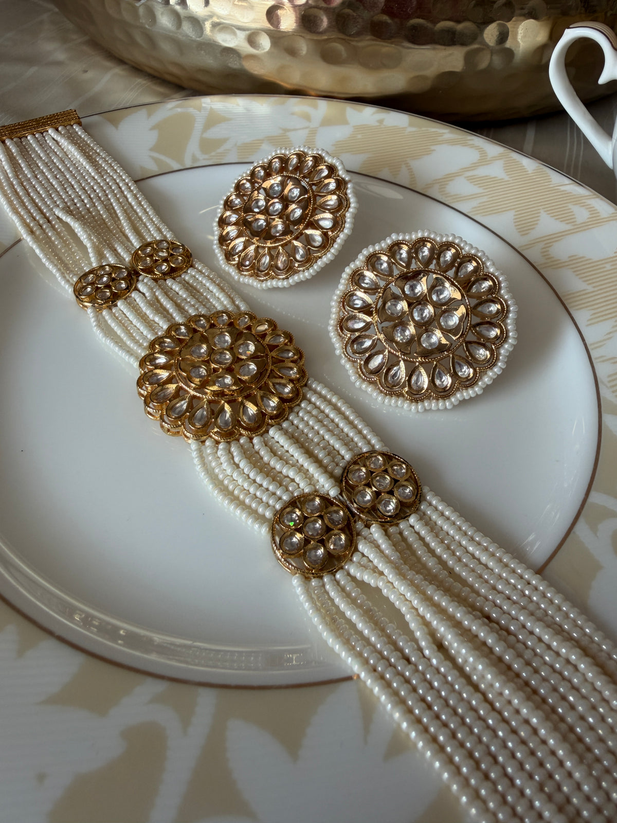 Angled view of the Renuka multi-strand pearl choker and matching clear-stone stud earrings