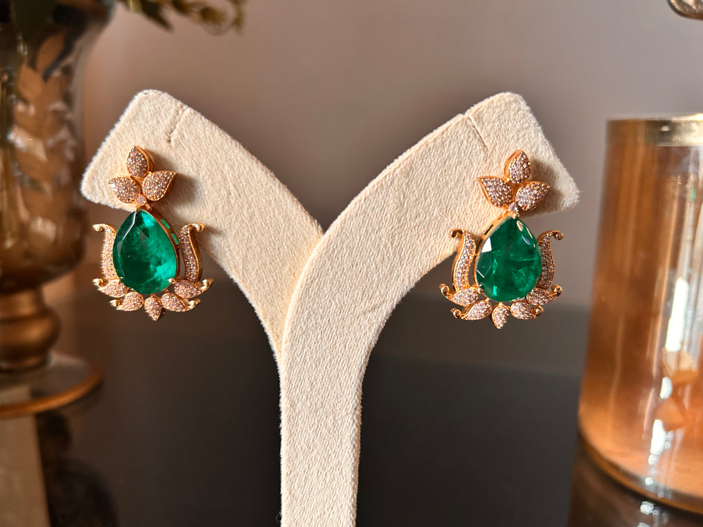 Close view of the Gul earring pair on a cream display, with green teardrop stones, clear-stone leaf motifs and gold-tone borders.