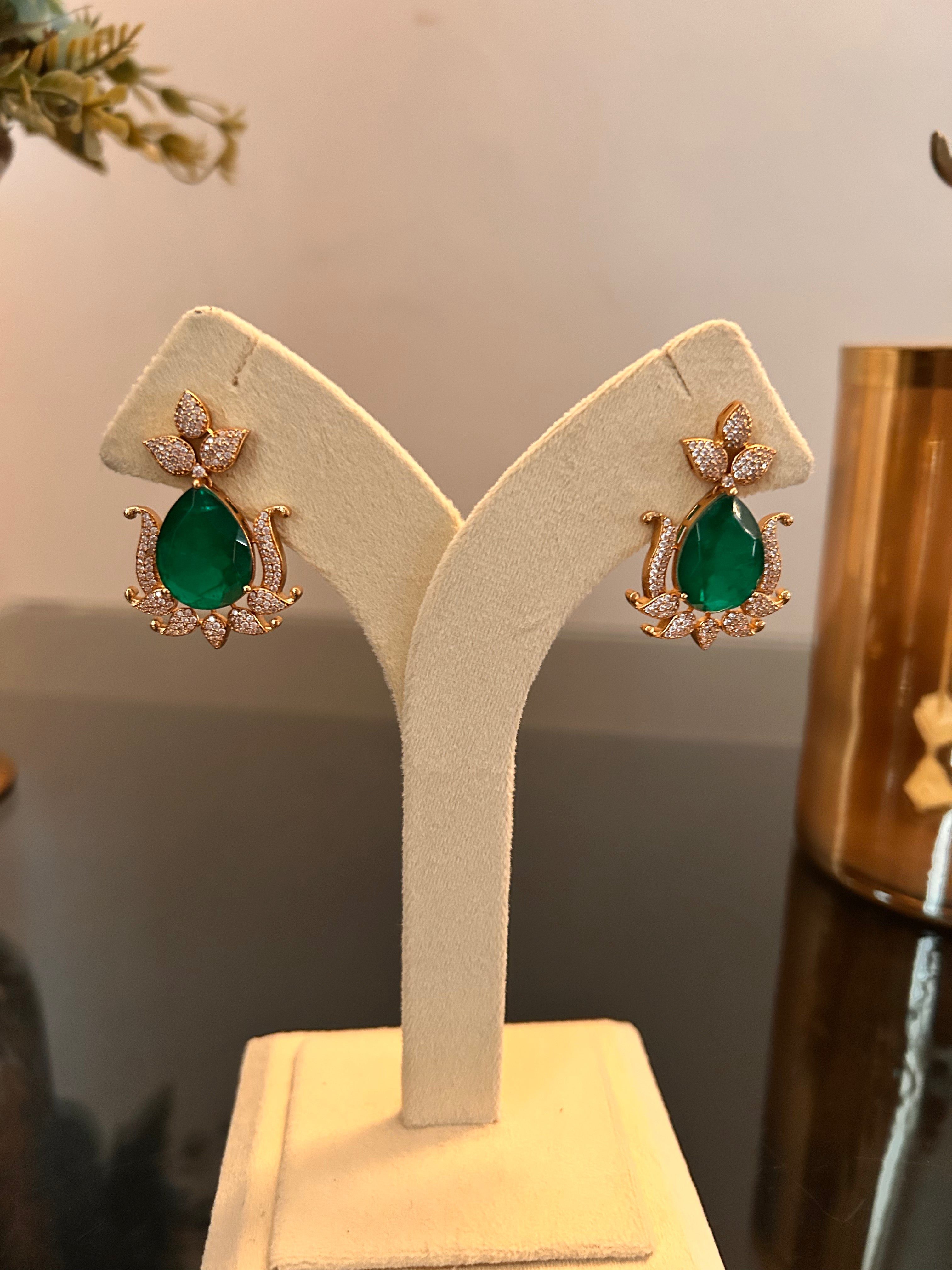 Gul green-stone earrings shown together on a full cream jewellery stand, with clear-stone detailing and gold-tone settings.
