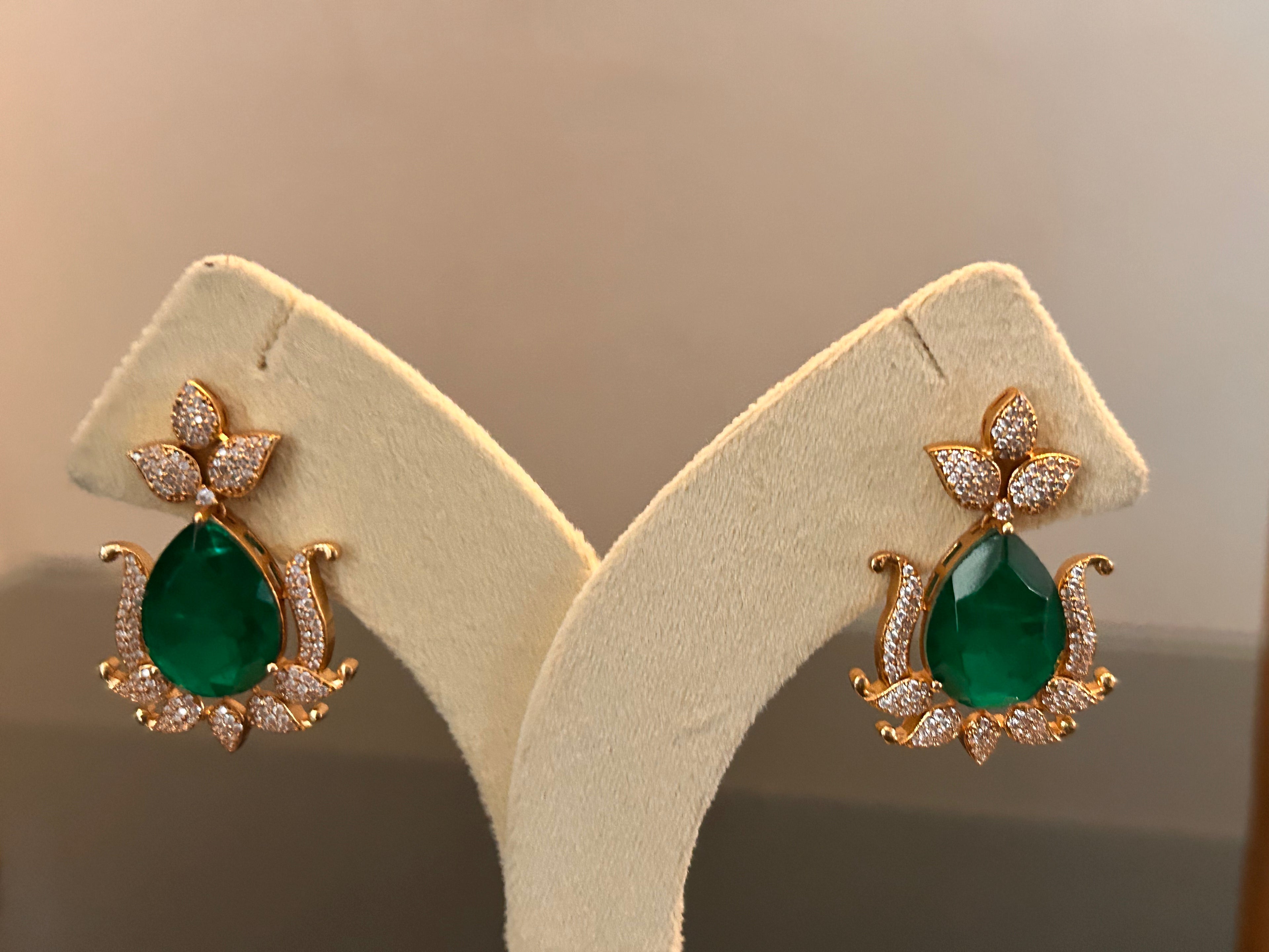 Front view of Gul green teardrop earrings hanging on a cream stand, showing the clear-stone floral tops and gold-tone settings.