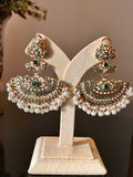 Front view of Khwahish earrings on a cream stand, showing green and pink stones, gold-tone fan-shaped details and pearl-like fringes.
