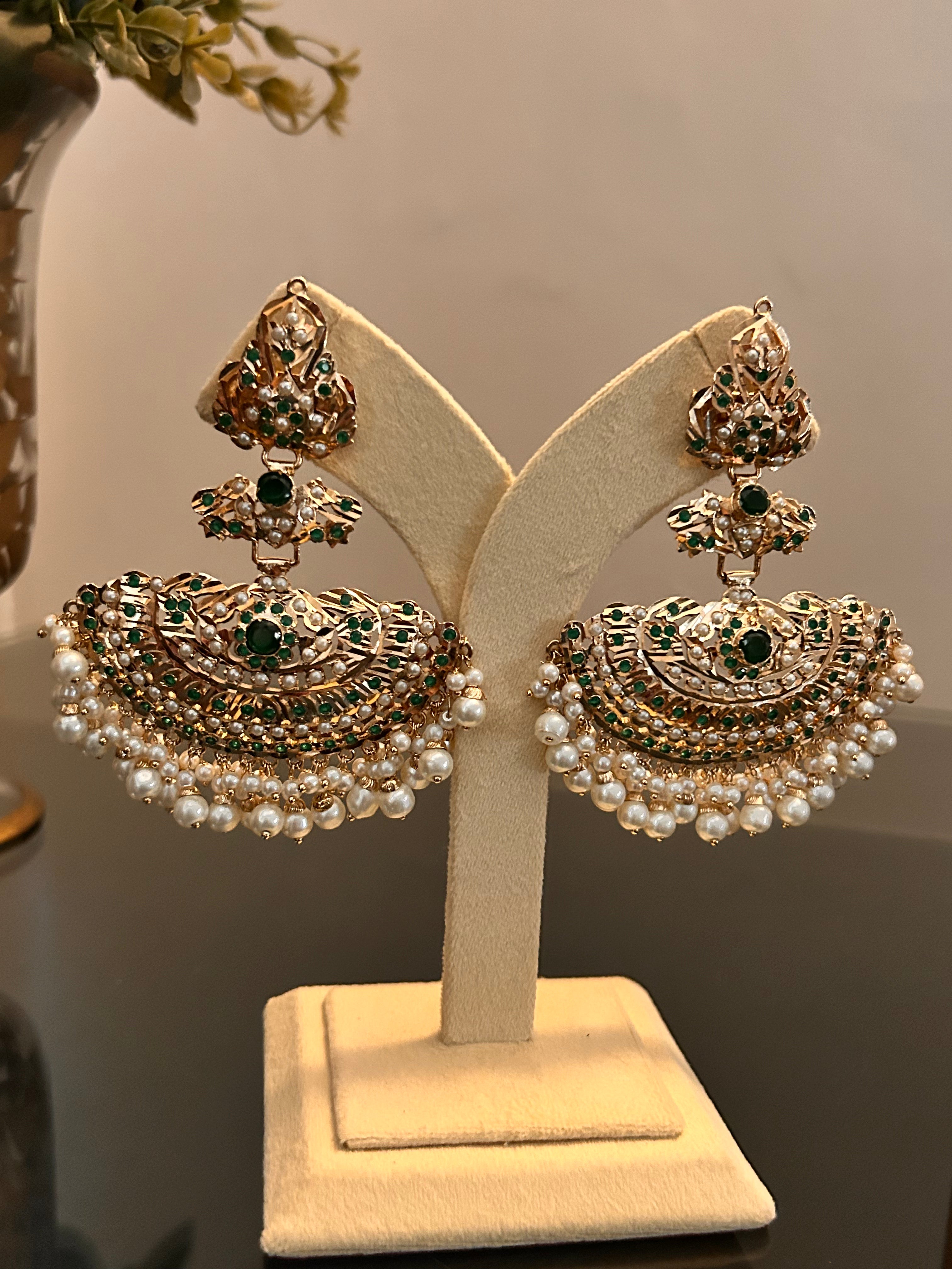 Full view of Khwahish earrings displayed on a cream stand in warm light, with green stone centres and pearl-like fringes.