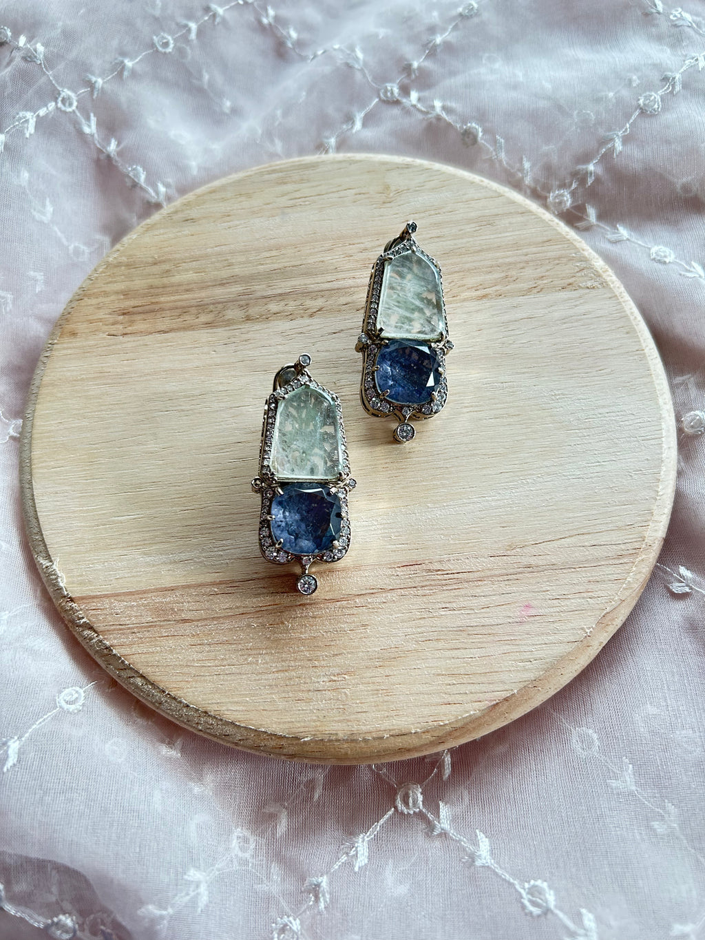 Inaara earrings shown as a matching pair, with pale doublet stones, blue stones and silver-tone settings on a wooden display.
