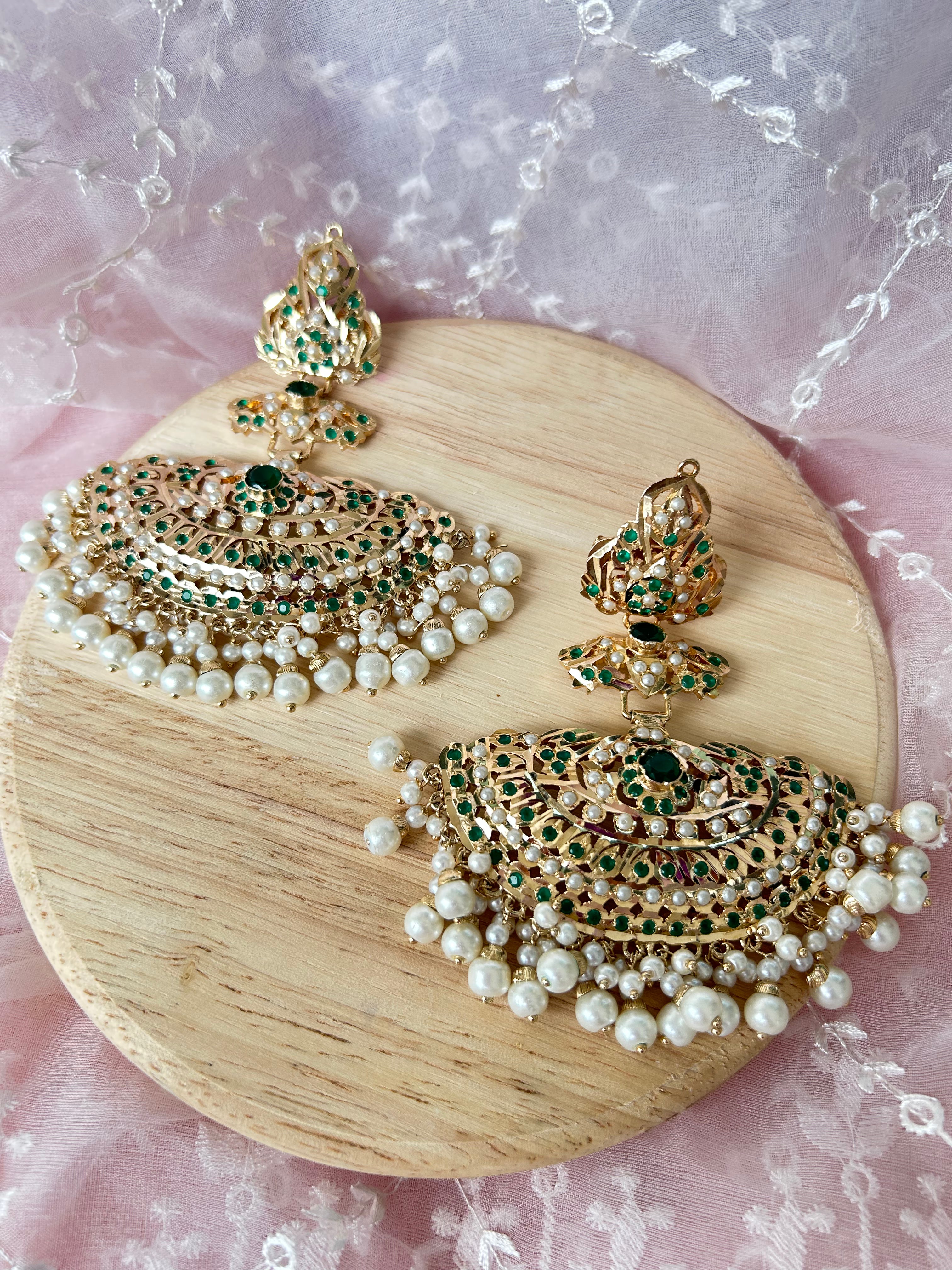 Khwahish earrings with green and pink stones and pearl-like fringes, shown as a pair on a round wooden display.