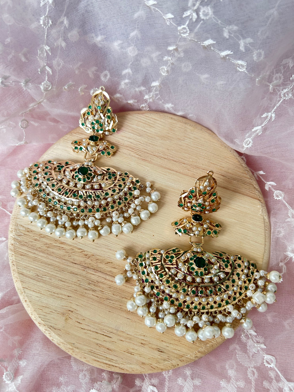 Khwahish earrings laid side by side on a wooden board, showing green and pink stones, gold-tone settings and pearl-like fringes.