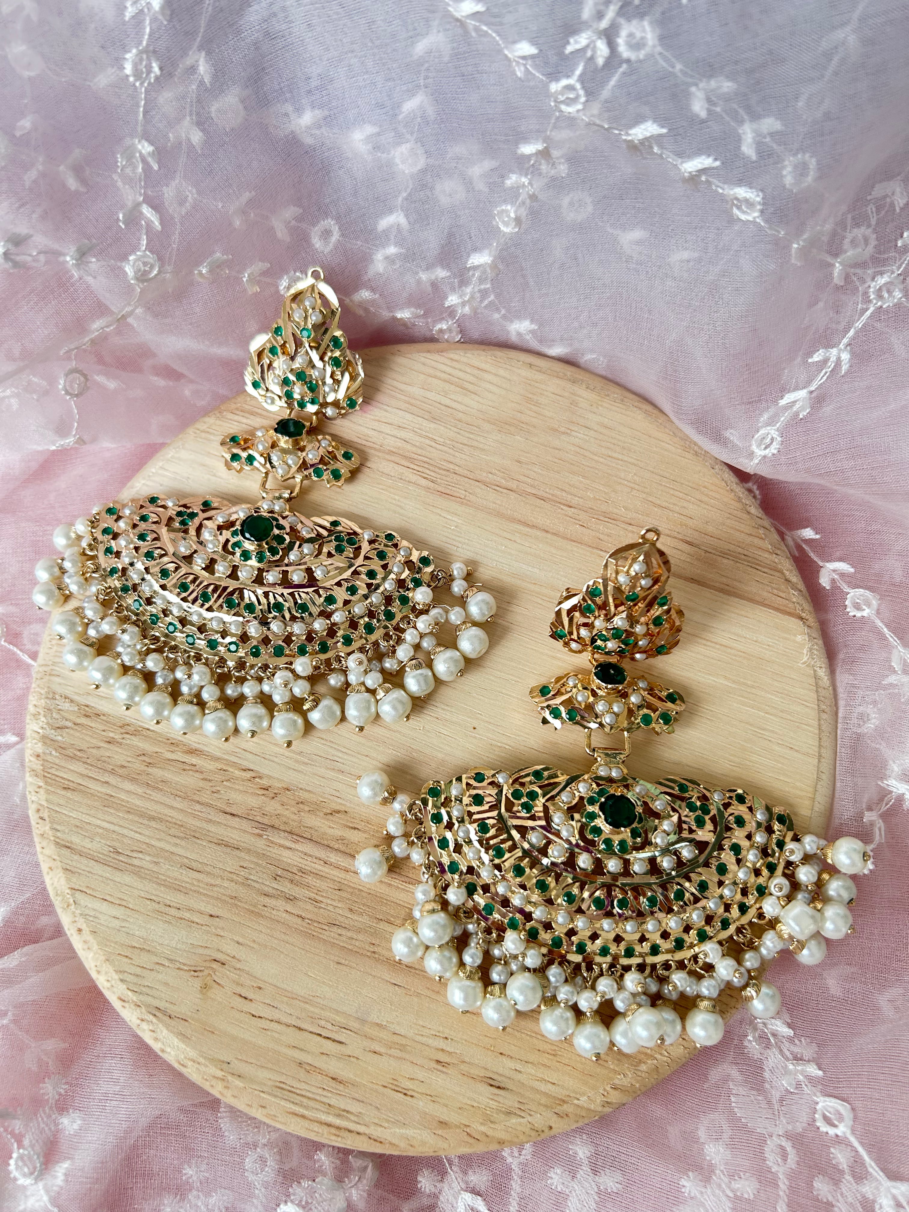 Khwahish earrings laid side by side on a wooden board, showing green and pink stones, gold-tone settings and pearl-like fringes.
