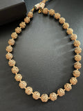Maira brass carved-bead necklace arranged on a dark surface beside a KINAHH box, showing the textured round beads.