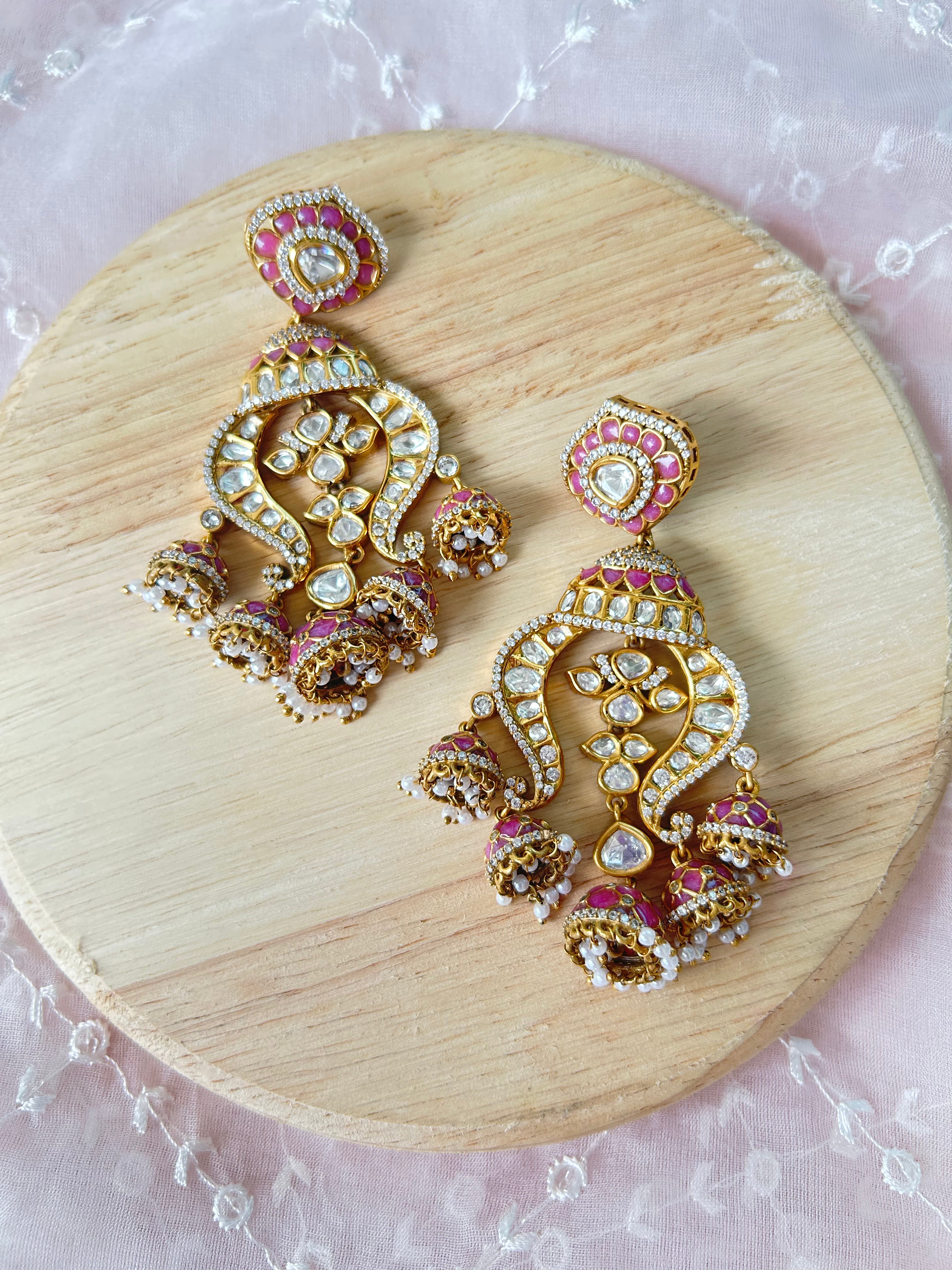 Noor chandelier earrings with pink enamel, clear polki stones and pearl-like drops, shown as a pair on a wooden display.