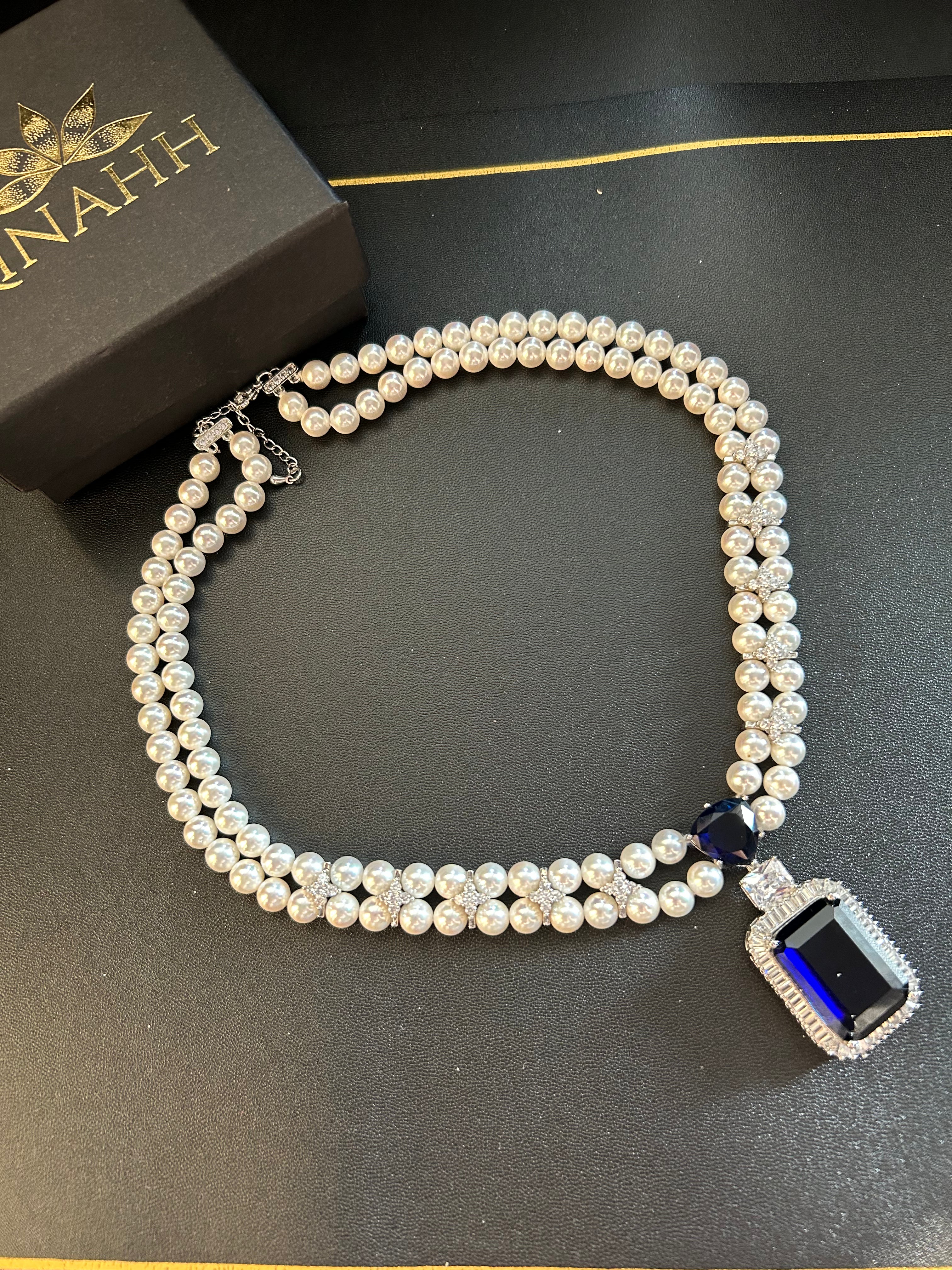 Rhea Necklace detail view showing shell pearls and a blue stone pendant.