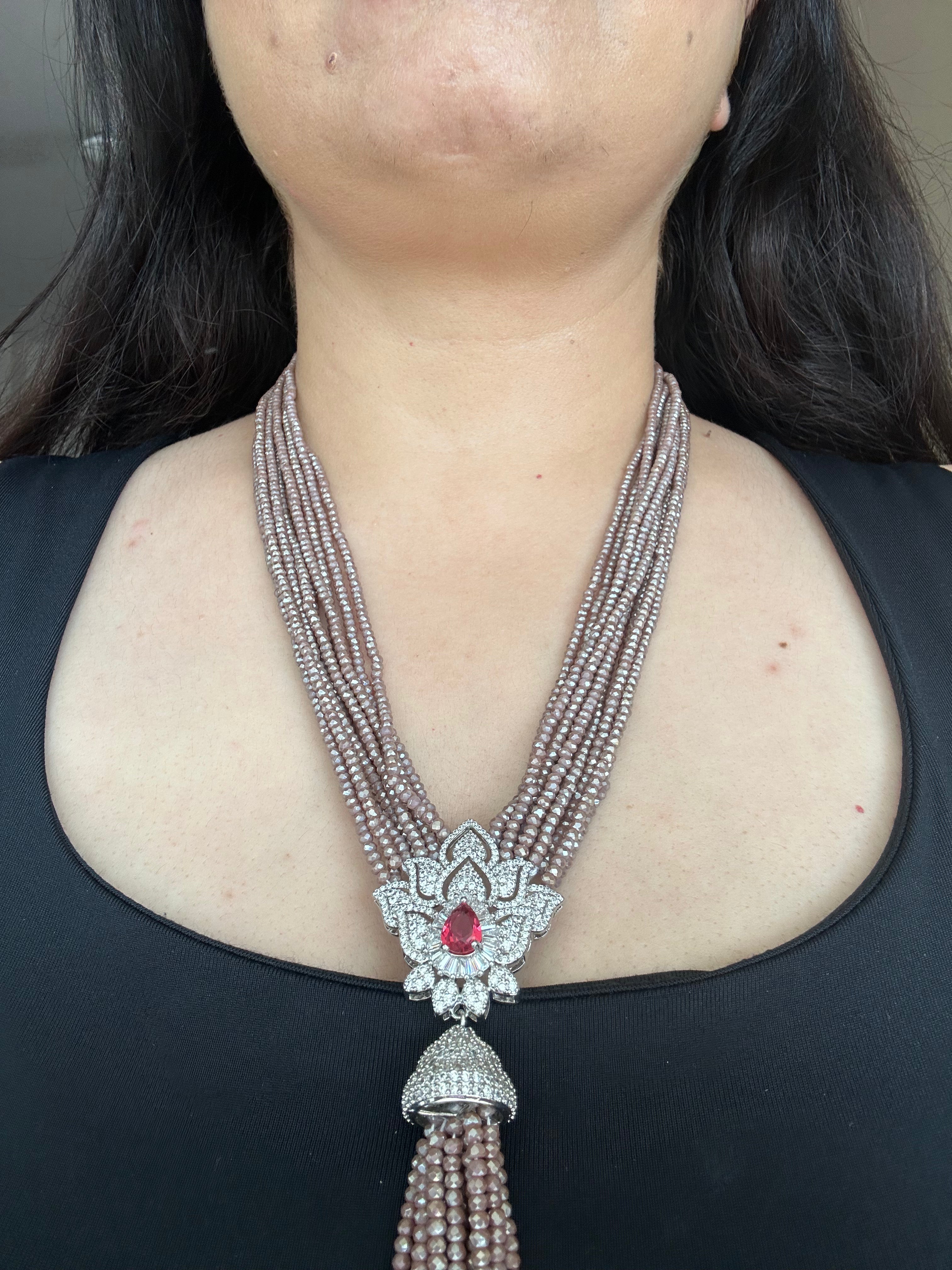 Close worn view of Adaa Necklace, showing its multiple bead strands and red-centred floral pendant.