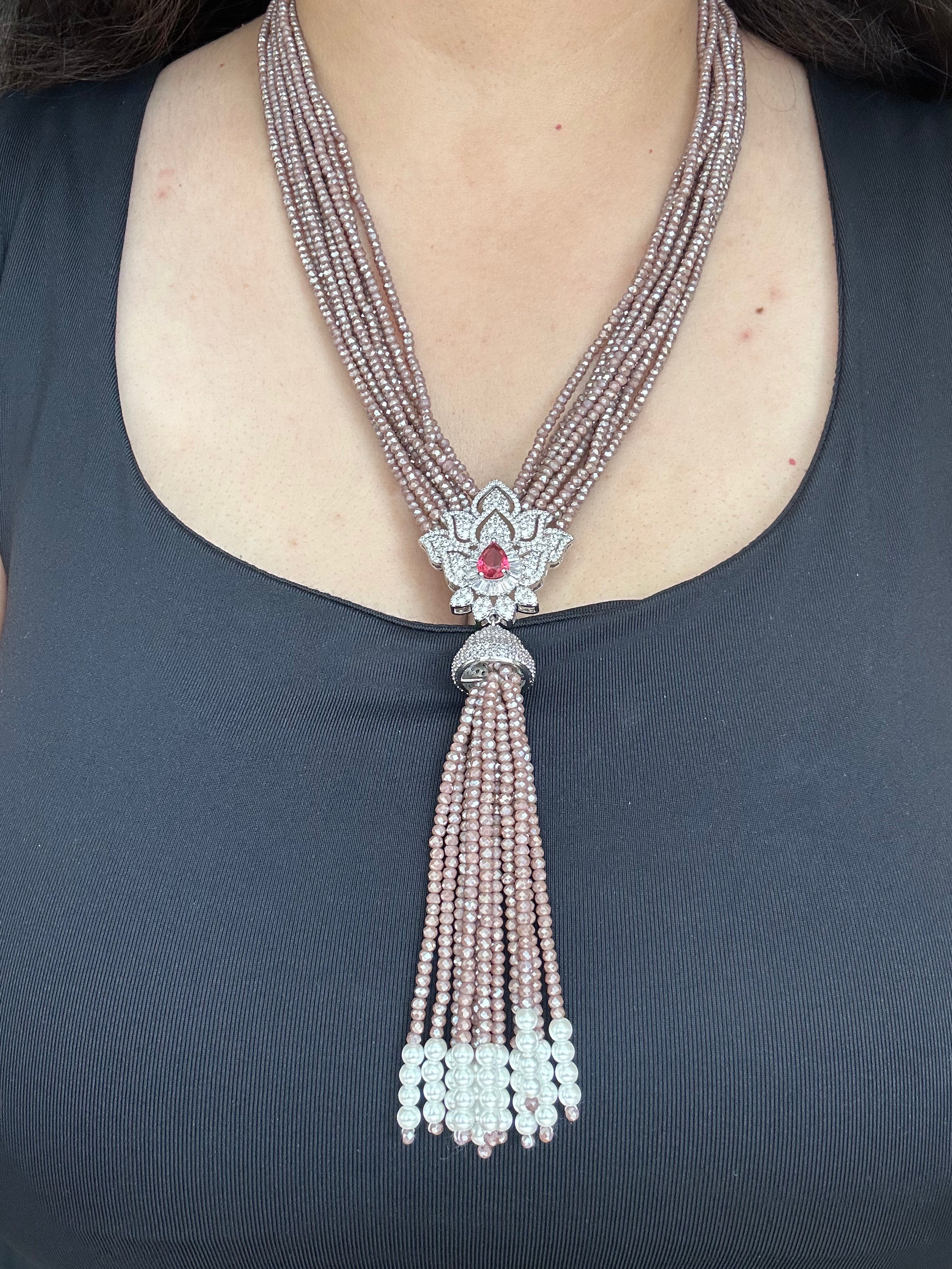 Adaa Necklace worn against a dark top, with a red-centred pendant and long white-tipped tassel.
