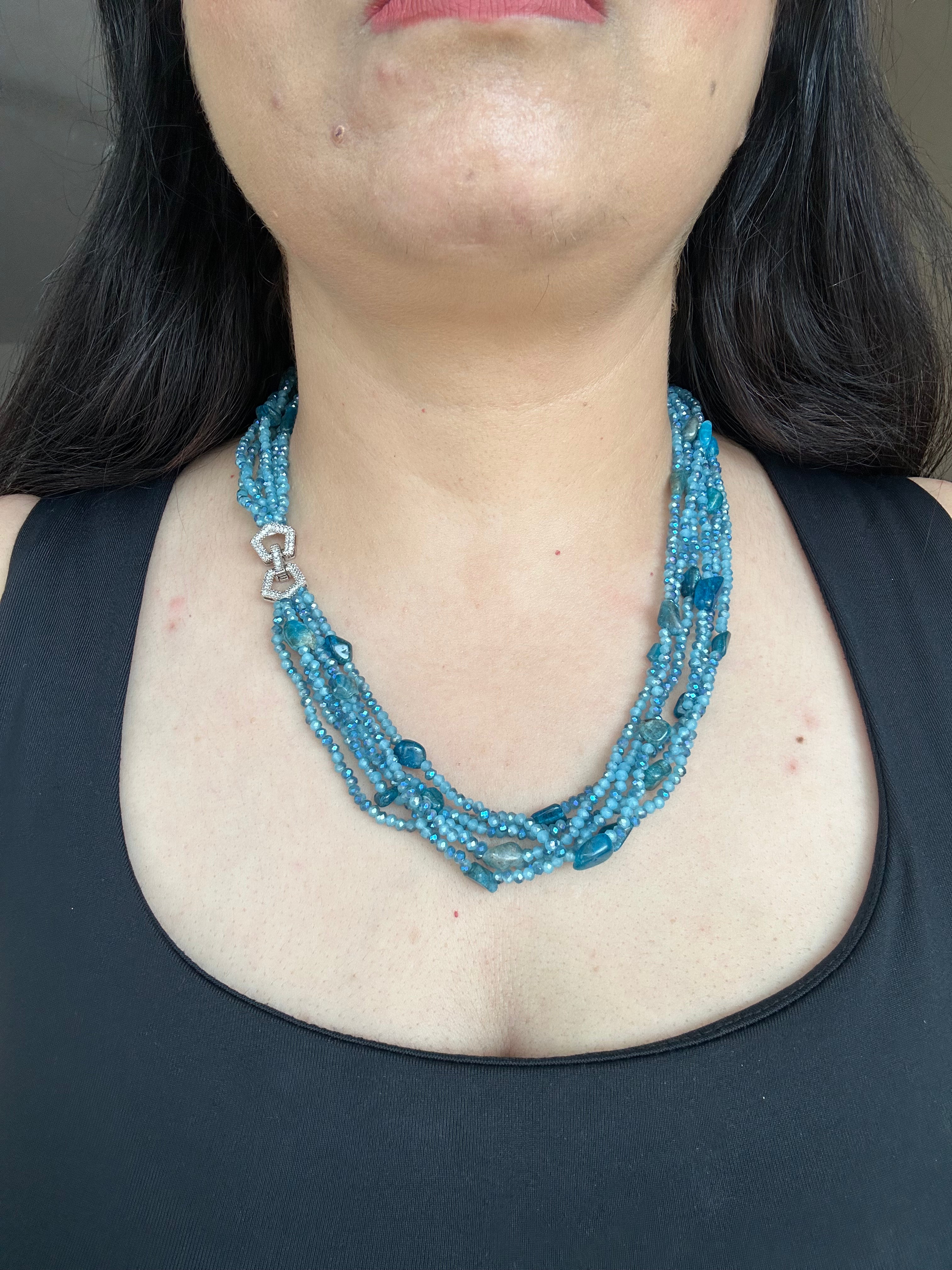 Evara Necklace in turquoise, worn against a dark top with multiple bead strands and a clear-stone linked clasp.