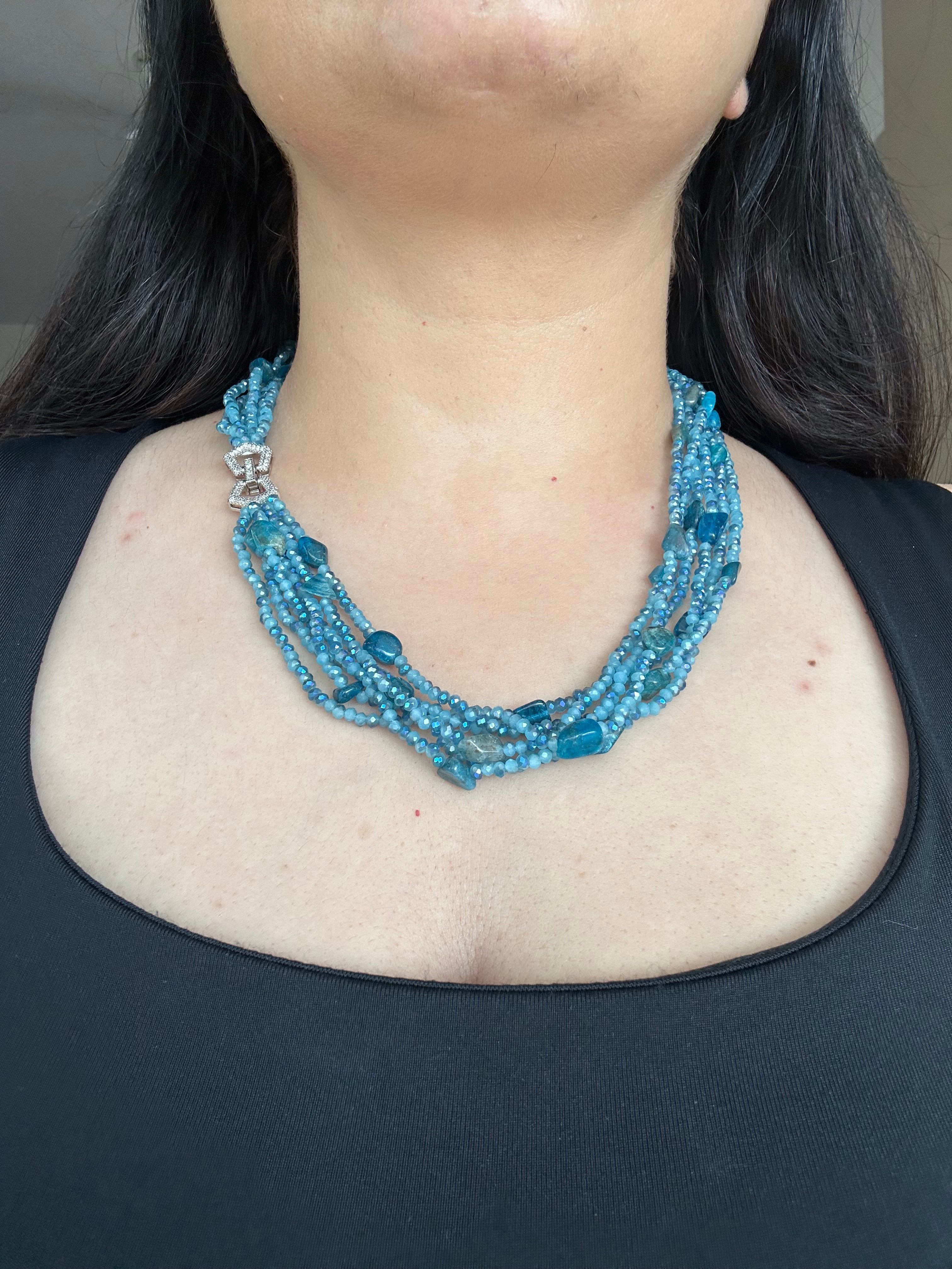 Evara Necklace in turquoise, worn against a dark top with multiple bead strands and a clear-stone linked clasp.