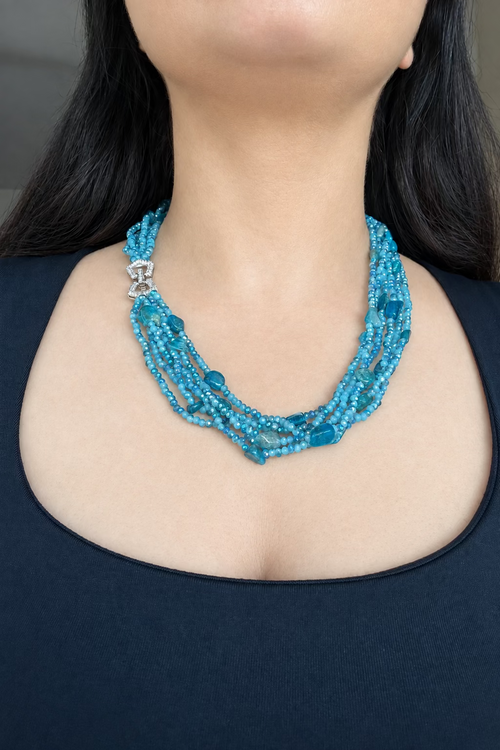 Evara Necklace in turquoise, worn against a dark top with multiple bead strands and a clear-stone linked clasp.