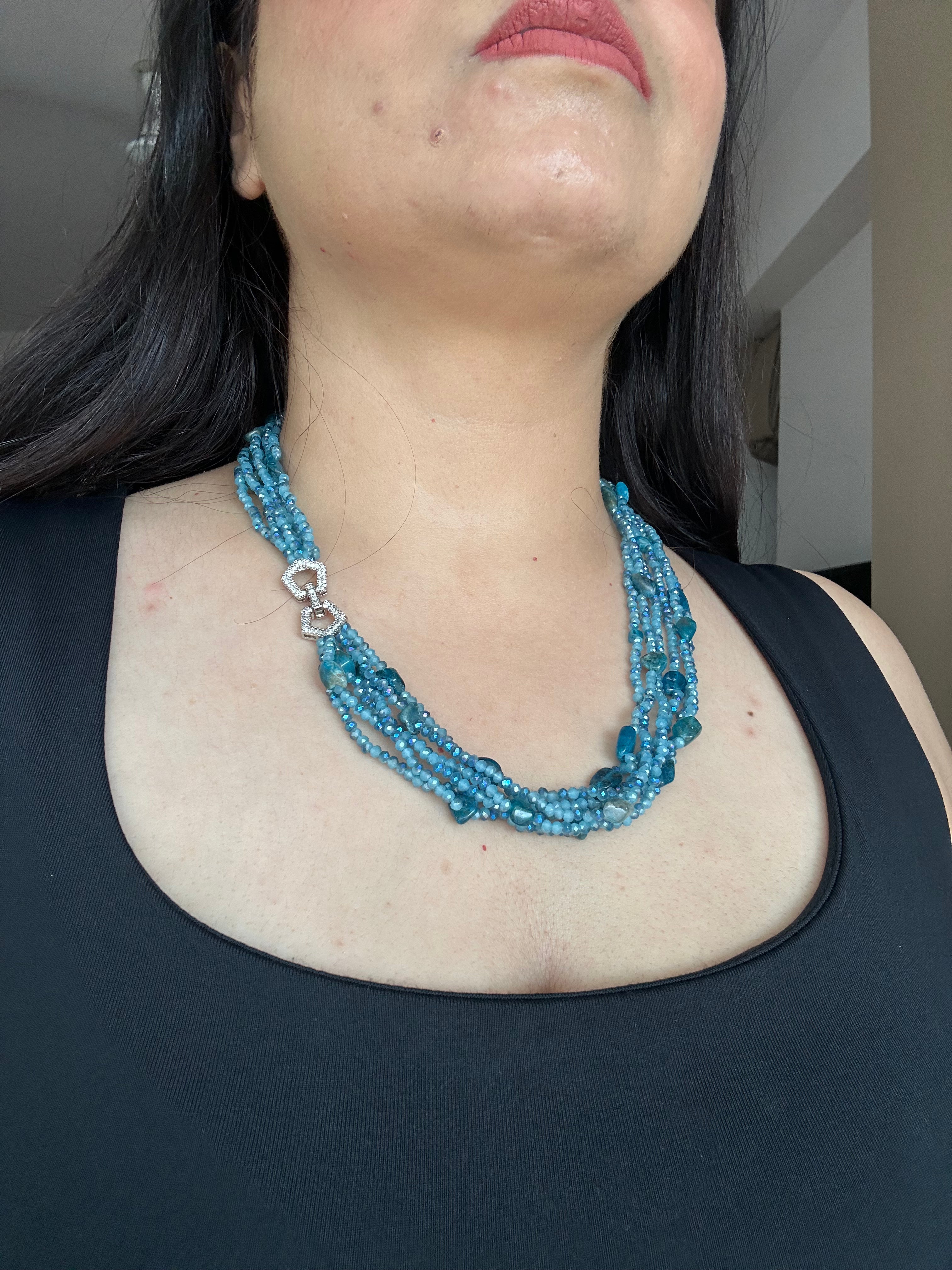 Evara Necklace in turquoise, worn against a dark top with multiple bead strands and a clear-stone linked clasp.
