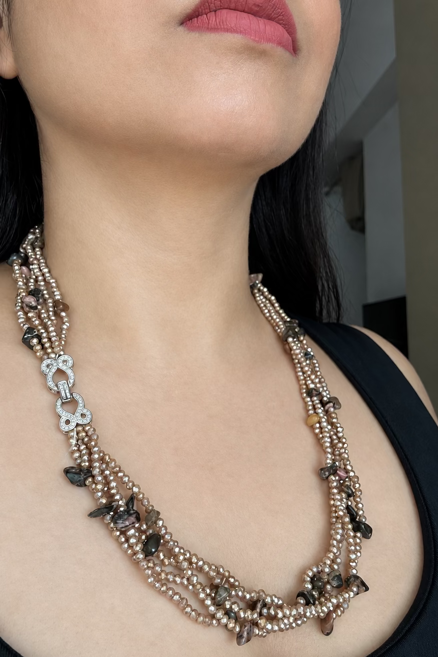 Evara Necklace in brown, worn against a dark top with multiple bead strands and a clear-stone linked clasp.