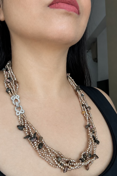 Evara Necklace in brown, worn against a dark top with multiple bead strands and a clear-stone linked clasp.