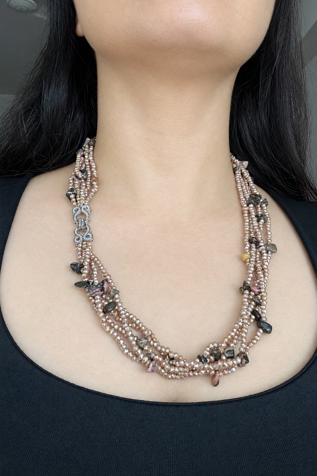 Evara Necklace in brown, worn against a dark top with multiple bead strands and a clear-stone linked clasp.