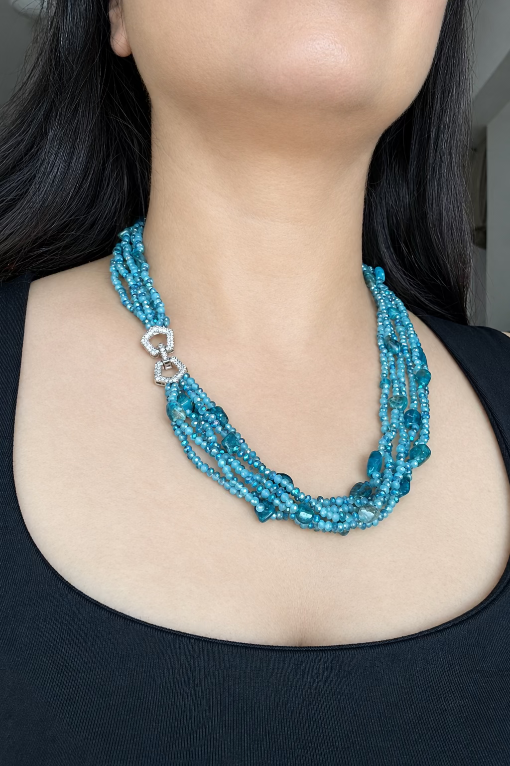 Evara Necklace in turquoise, worn against a dark top with multiple bead strands and a clear-stone linked clasp.