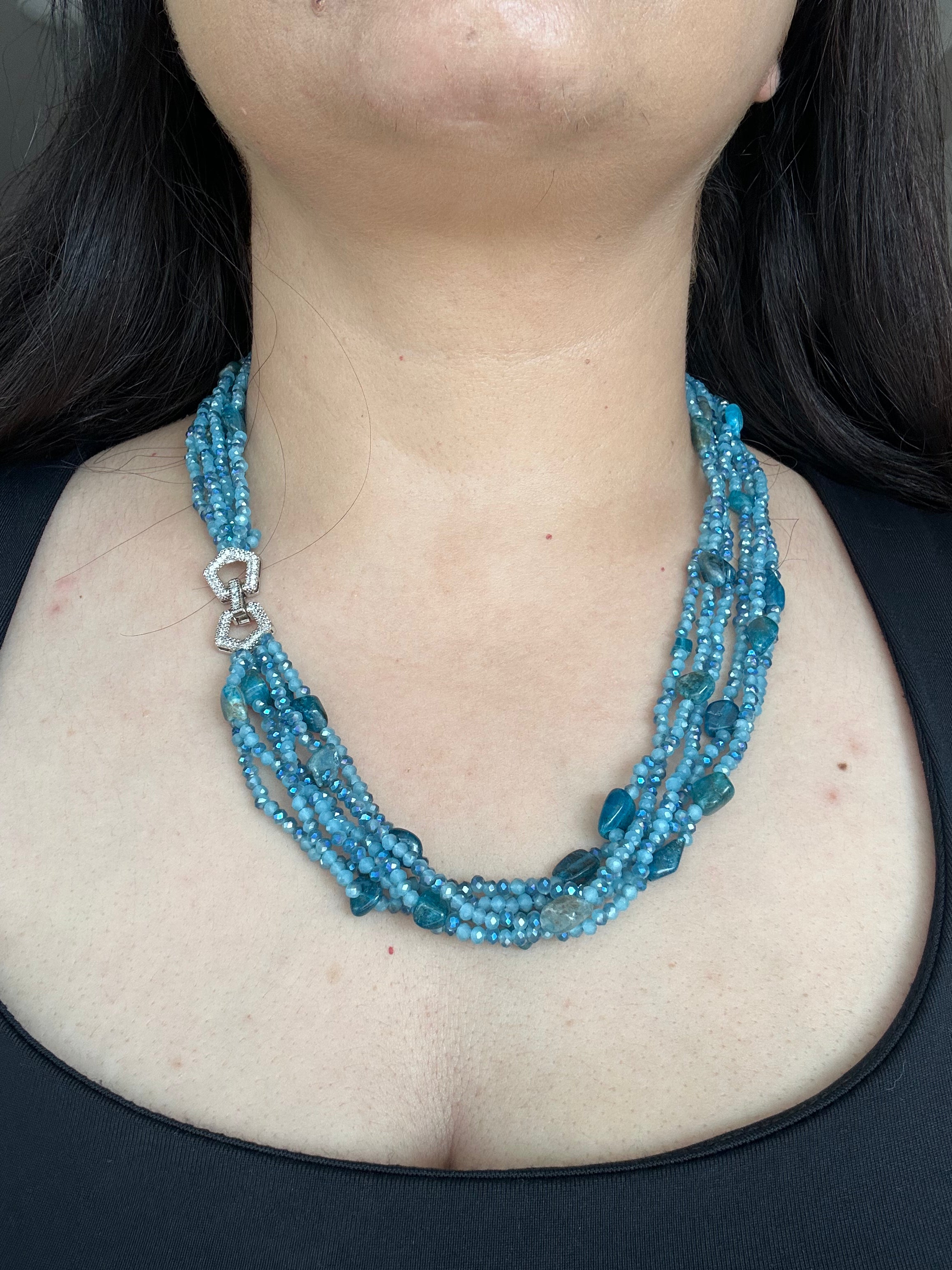 Evara Necklace by KINAHH in turquoise, worn from the front to show its layered bead strands and sparkling linked clasp.