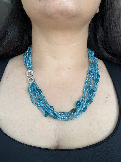 Evara Necklace by KINAHH in turquoise, worn from the front to show its layered bead strands and sparkling linked clasp.