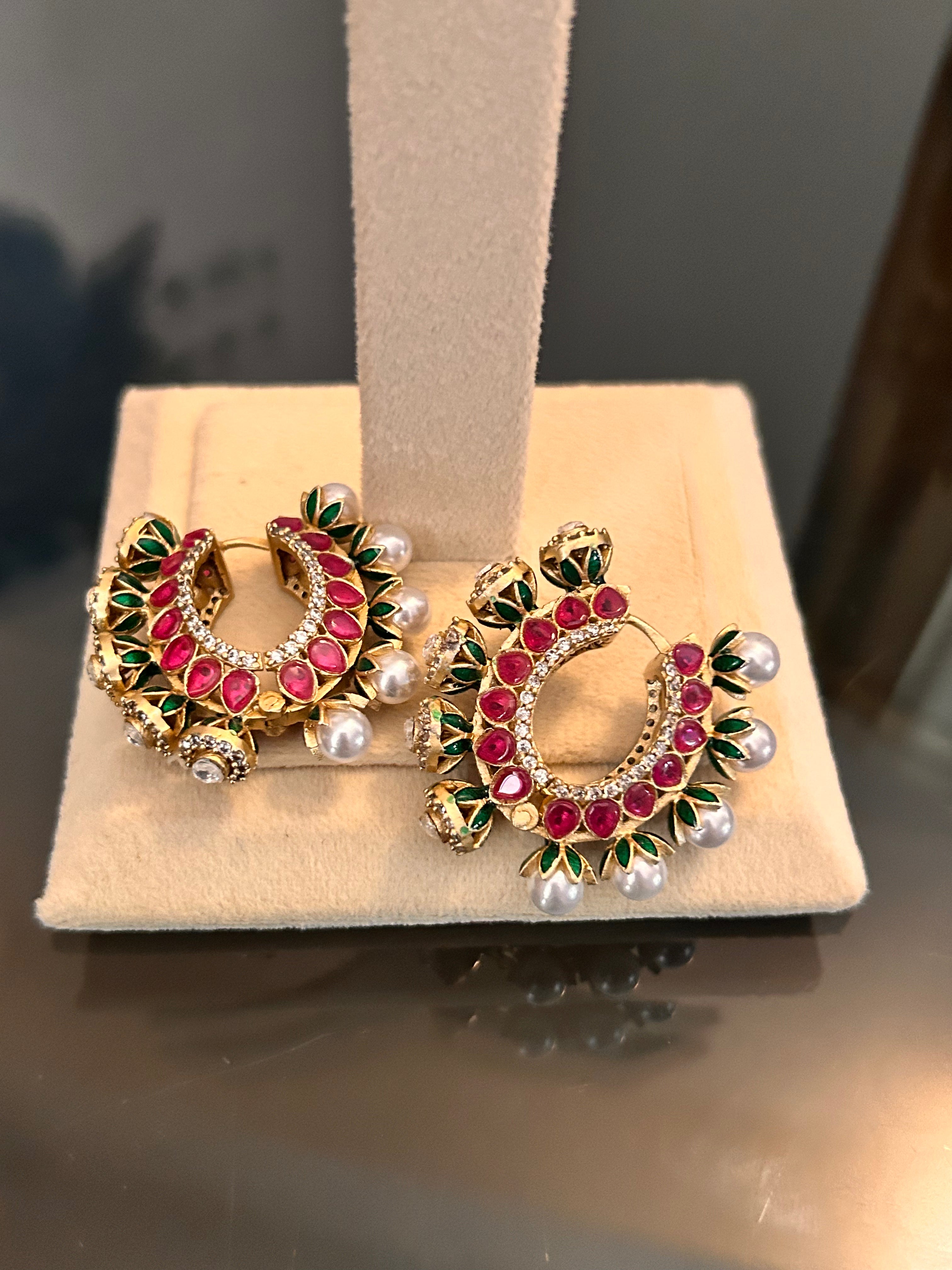 Gulnaar Hoops resting as a pair on a cream stand base, showing pink and green enamel and pearl-like drops.
