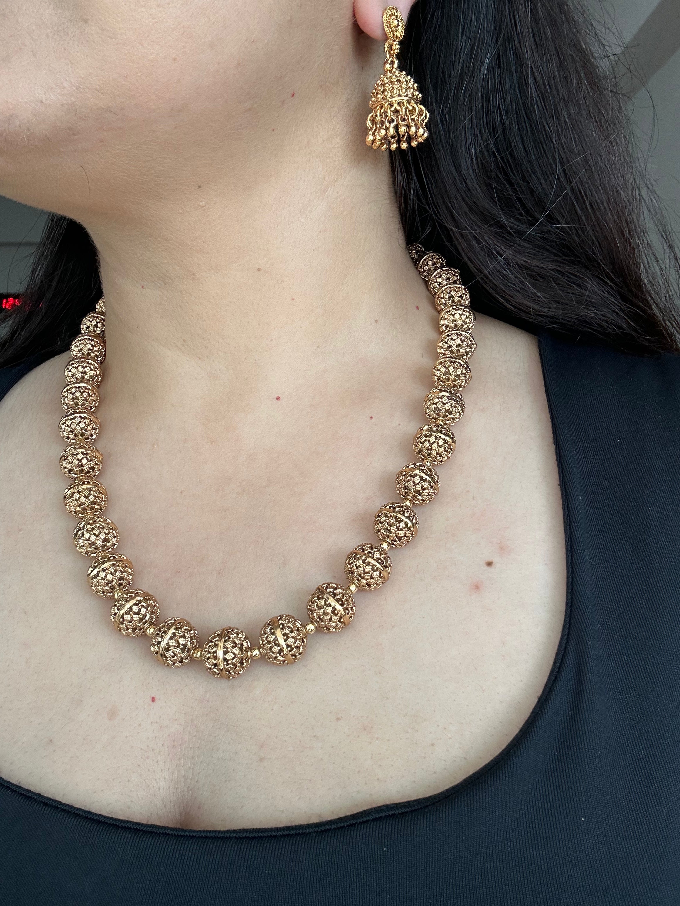 Side-angle worn view of Maira's carved-bead necklace and matching jhumka earring.