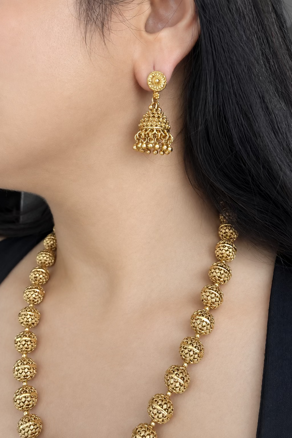 Close worn view of Maira's matching jhumka earring with part of the carved-bead necklace visible.