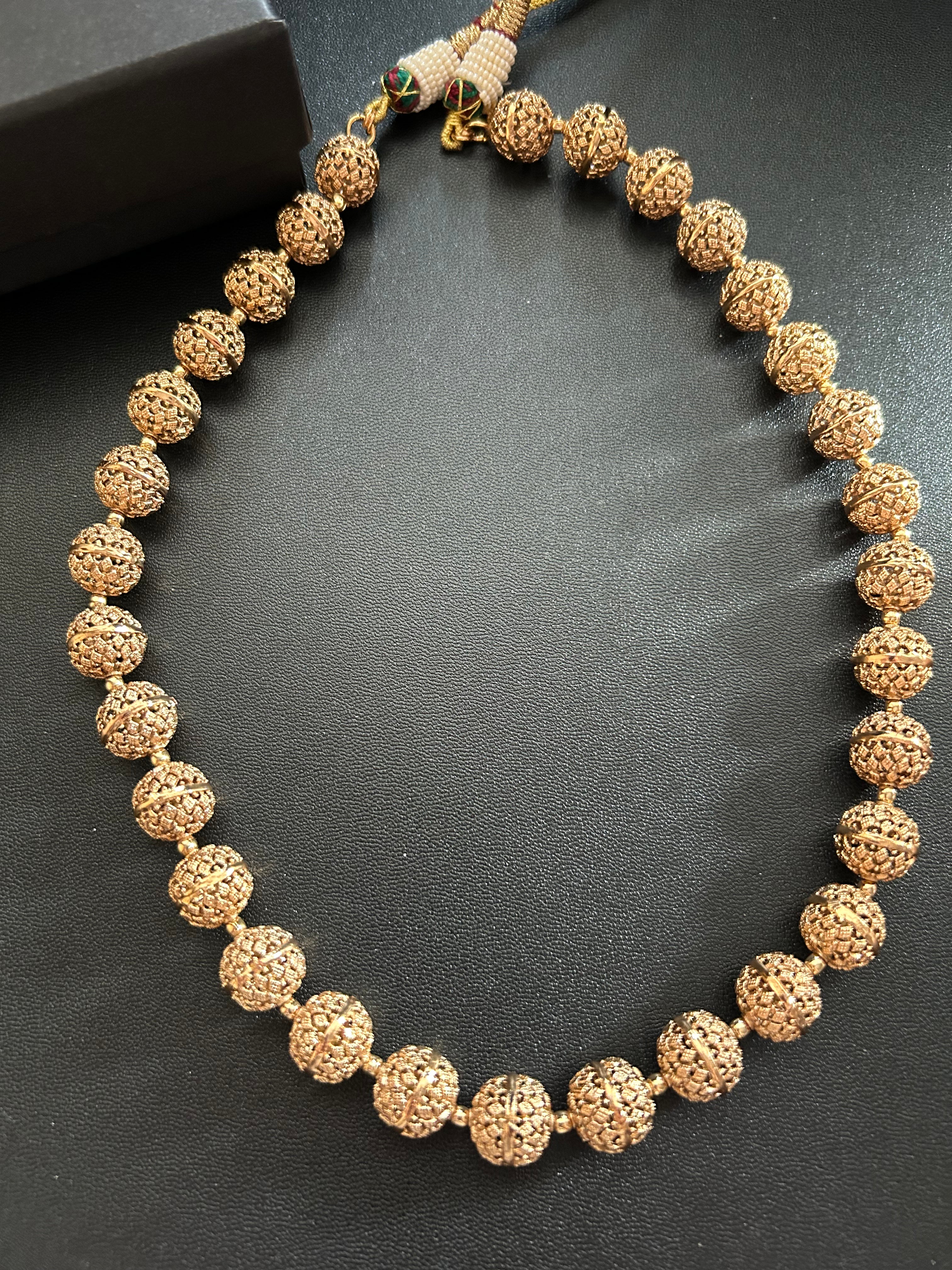 Maira carved-bead necklace laid flat on a dark surface beside a black KINAHH box.
