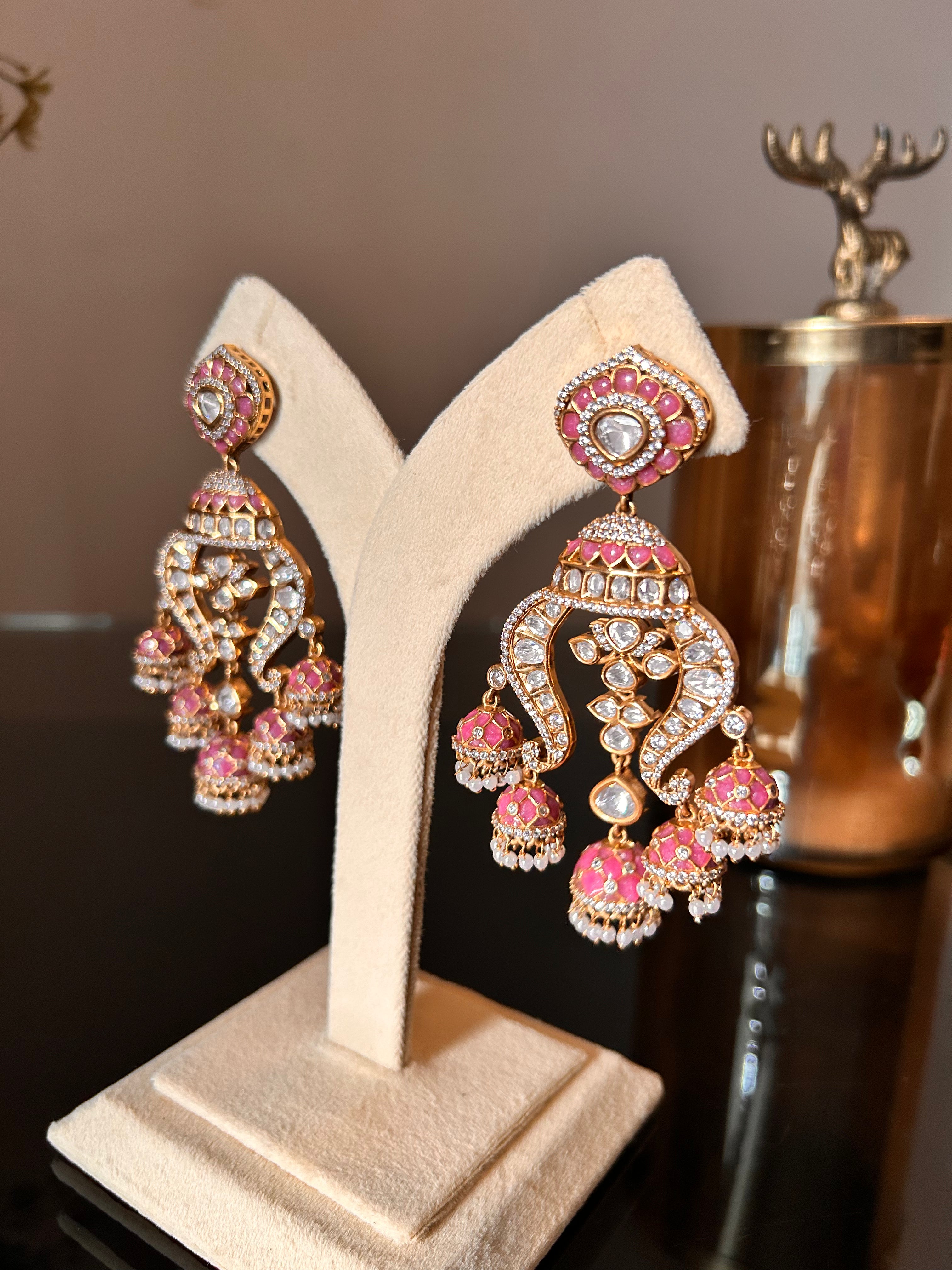 Angled view of Noor pink enamel earrings on a cream stand, showing the clear stonework and dangling pearl-like details.