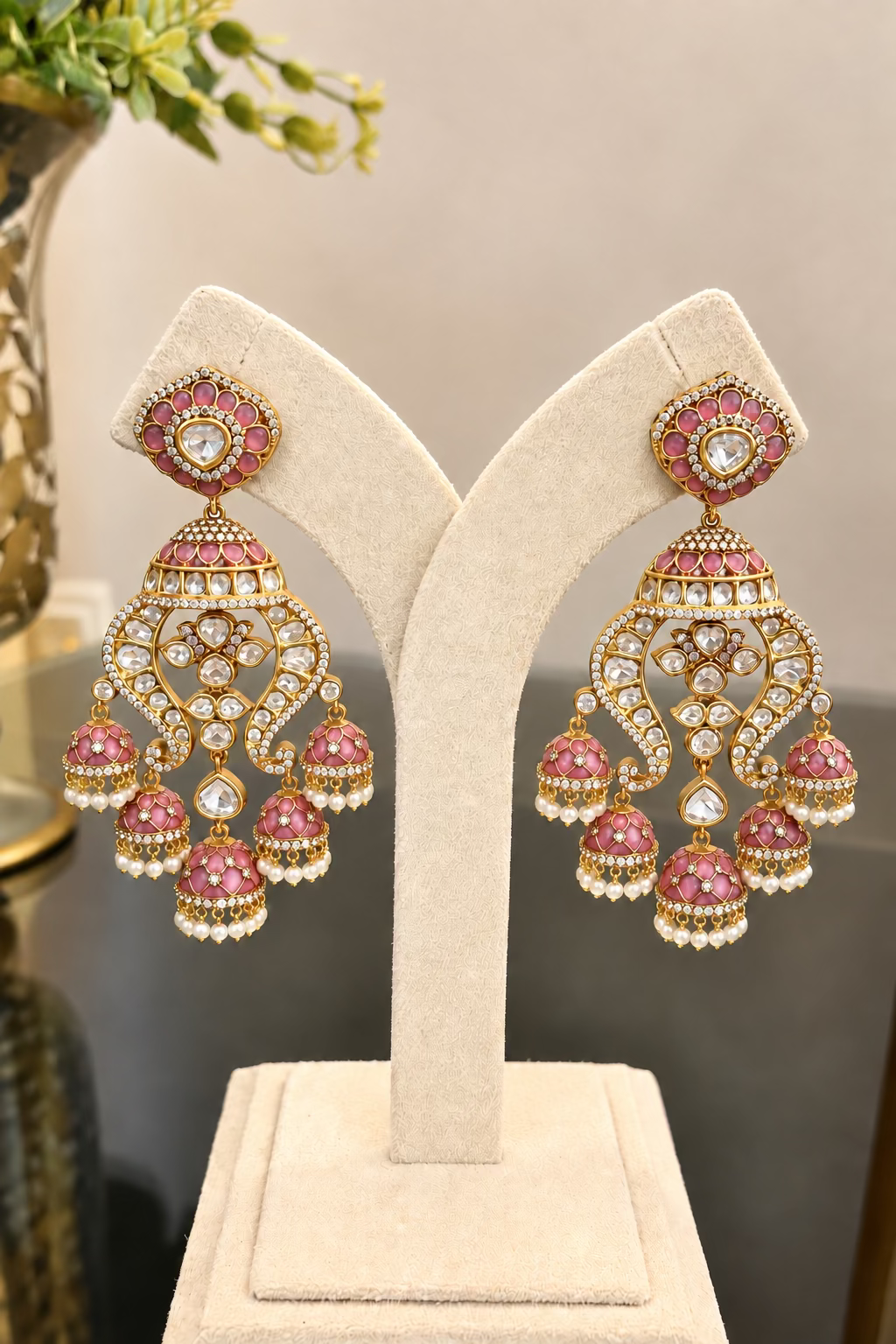 Full-pair view of Noor pink enamel and clear-stone earrings on a cream jewellery display stand.