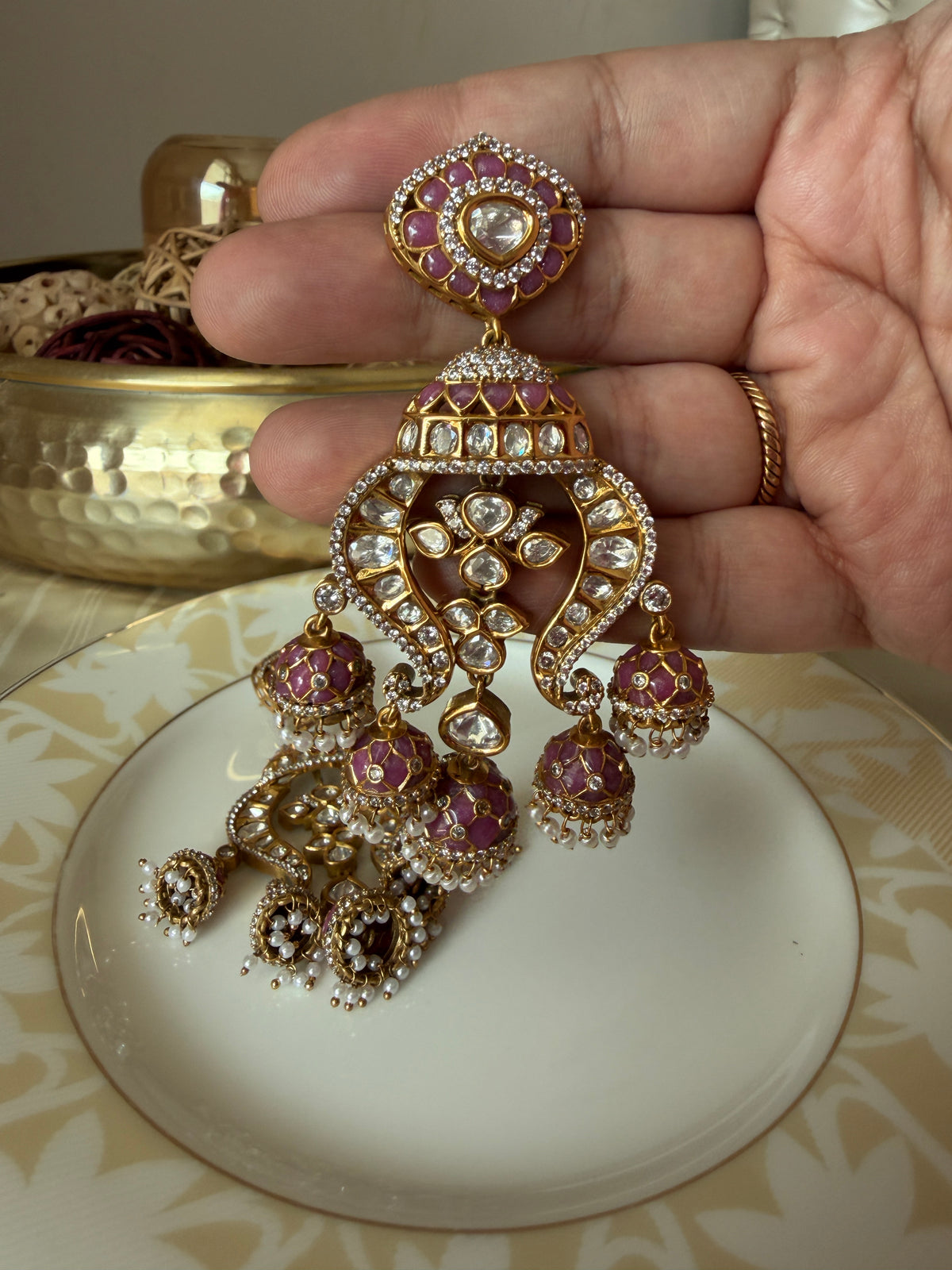 Close-up of a Noor earring held in hand, highlighting the pink enamel and ornate clear-stone design.
