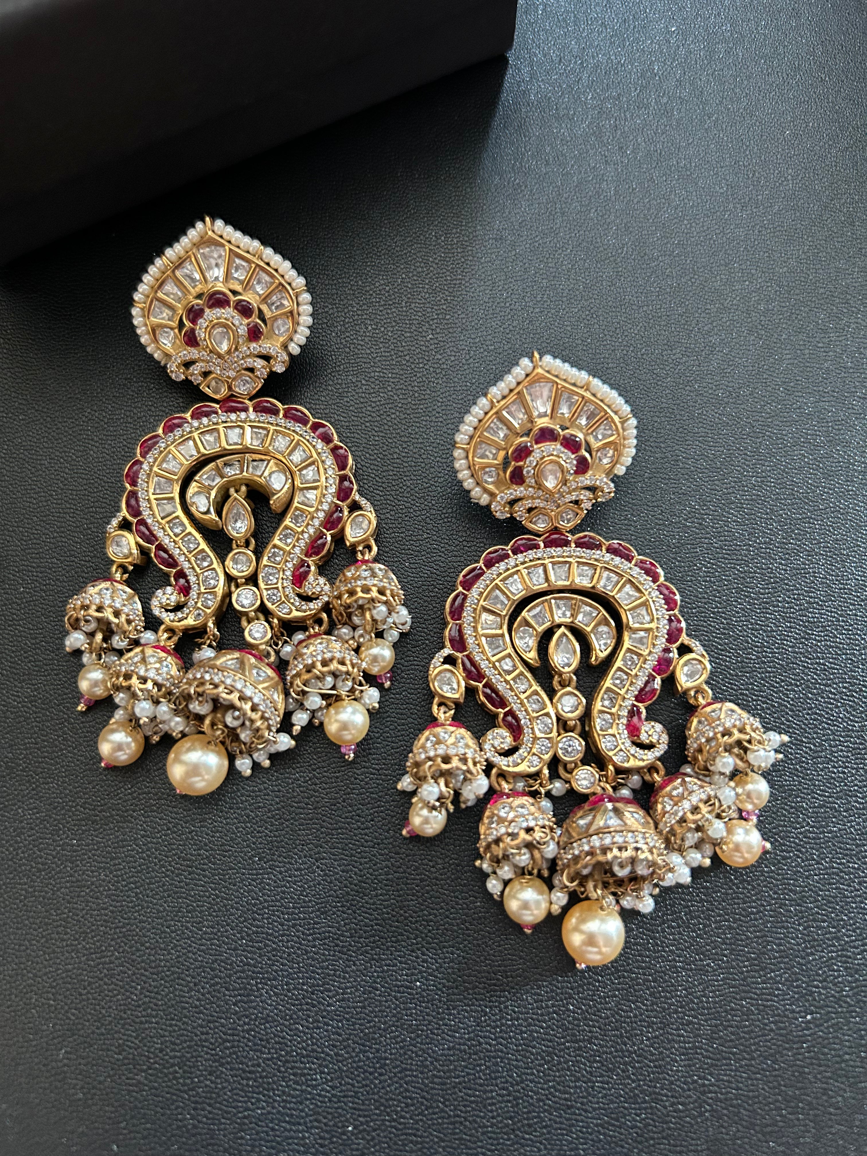Close front view of the Saanjh pair on a black surface, showing the intricate red and clear-stone setting.